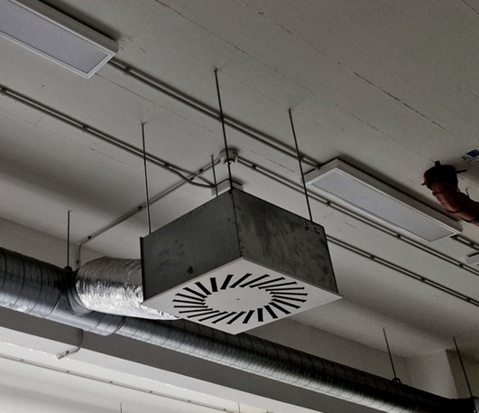 The photo shows an industrial HVAC system, including ductwork and air filters. The system provides air supply and exhaust, conditioning, and distribution throughout the building. Ventilation services